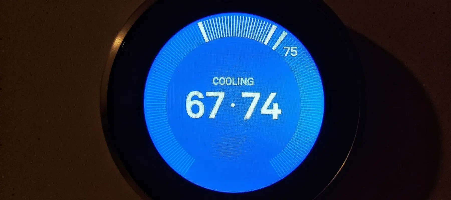 A digital thermostat displays COOLING with a current temperature of 74°F and a set temperature of 67°F on a bright blue screen.